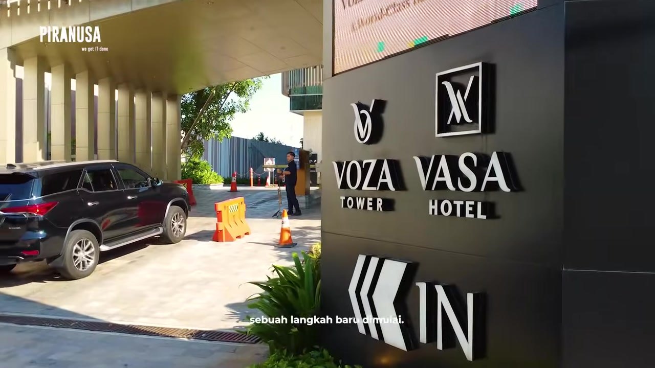 Papan nama Voza Tower dan Vasa Hotel di area masuk gedung dengan mobil terparkir